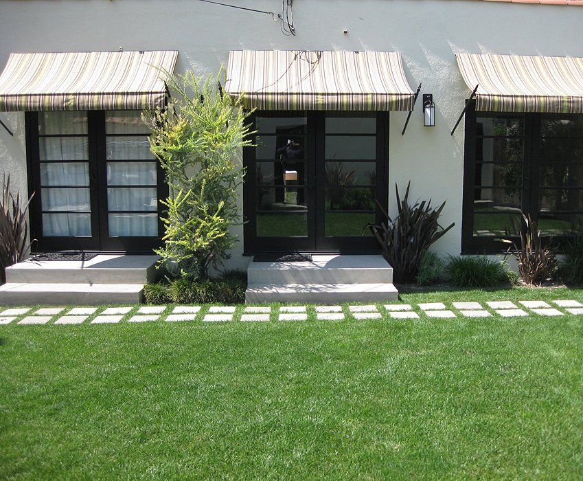 Modern house facade with striped awnings, black windows, and a green lawn with stepping stones.