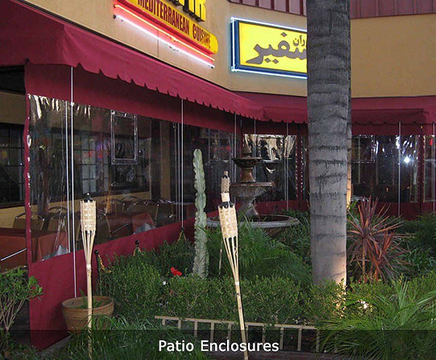 Outdoor patio enclosure with red awnings, glass walls, and potted plants beside a palm tree