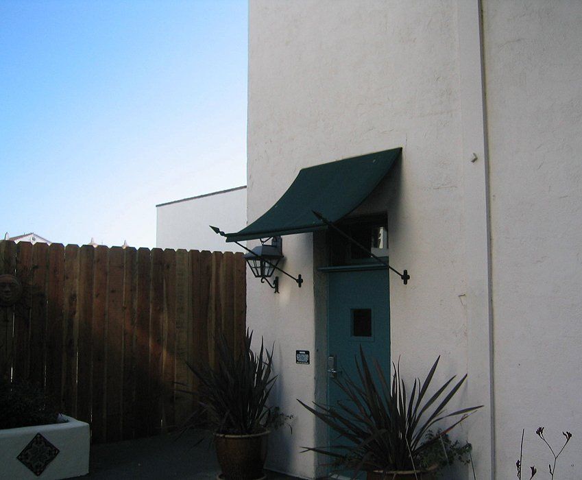 White building entrance with green awning and wall lights beside a wooden fence and plants