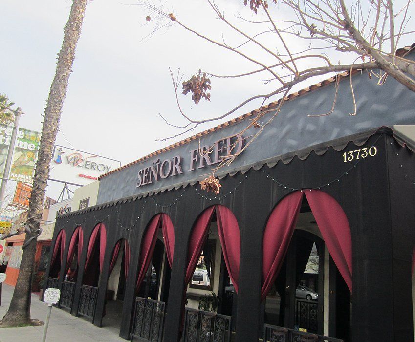 Storefront with black awning and burgundy arched curtains on a tree-lined street