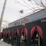 Dior store exterior with black facade, pink awnings, and bare tree branches overhead
