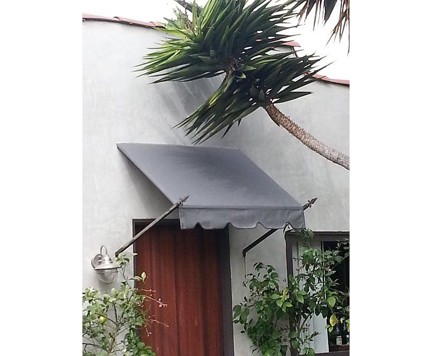White stucco house with a gray awning over a red door and greenery below a tree branch