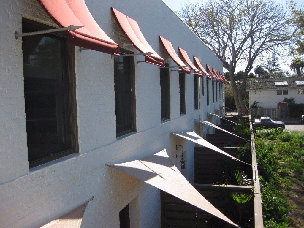 Side of a building with red awnings over windows and a shaded walkway along the wall