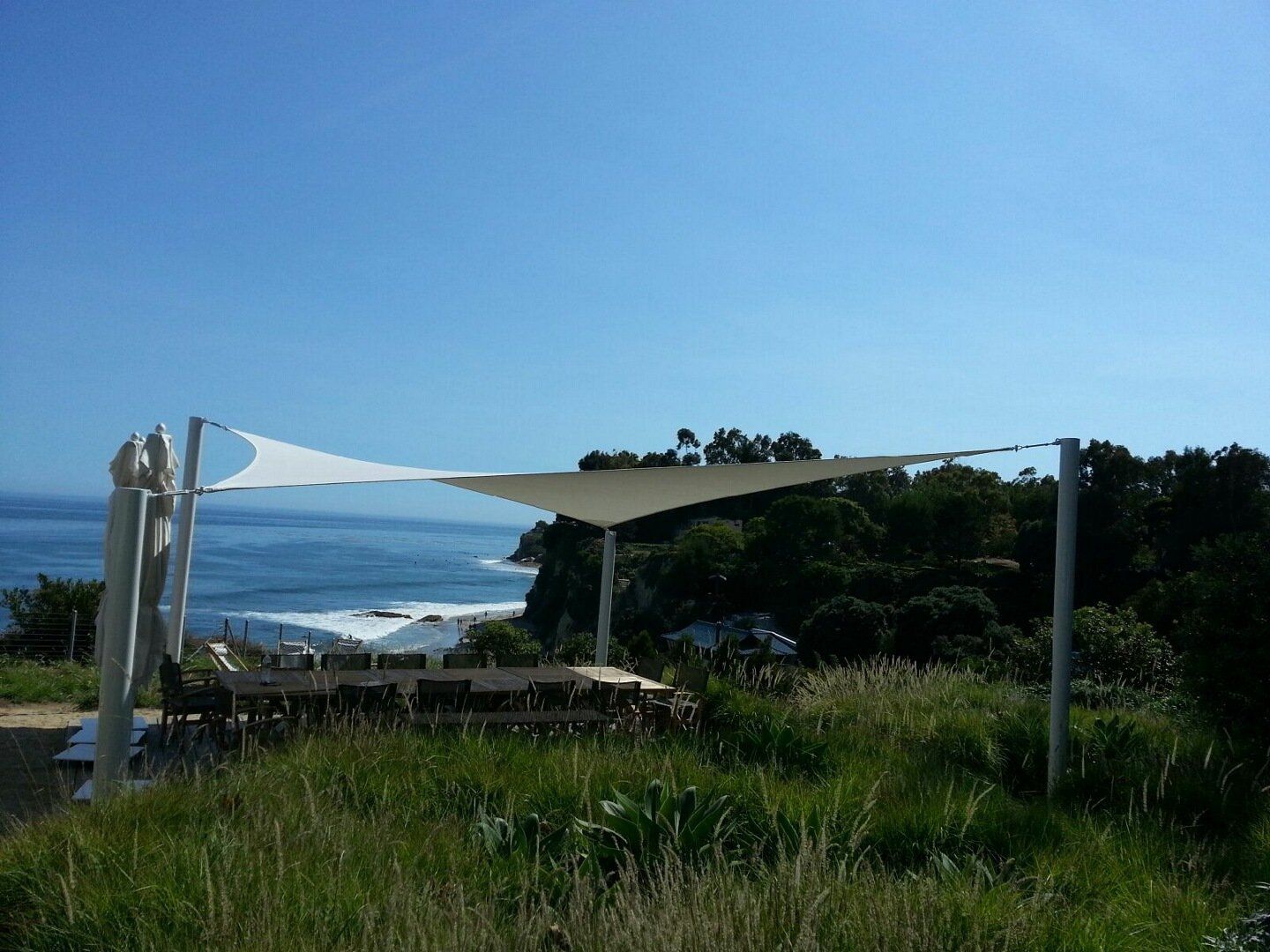 White shade canopy over a grassy seaside overlook with ocean and blue sky in the background