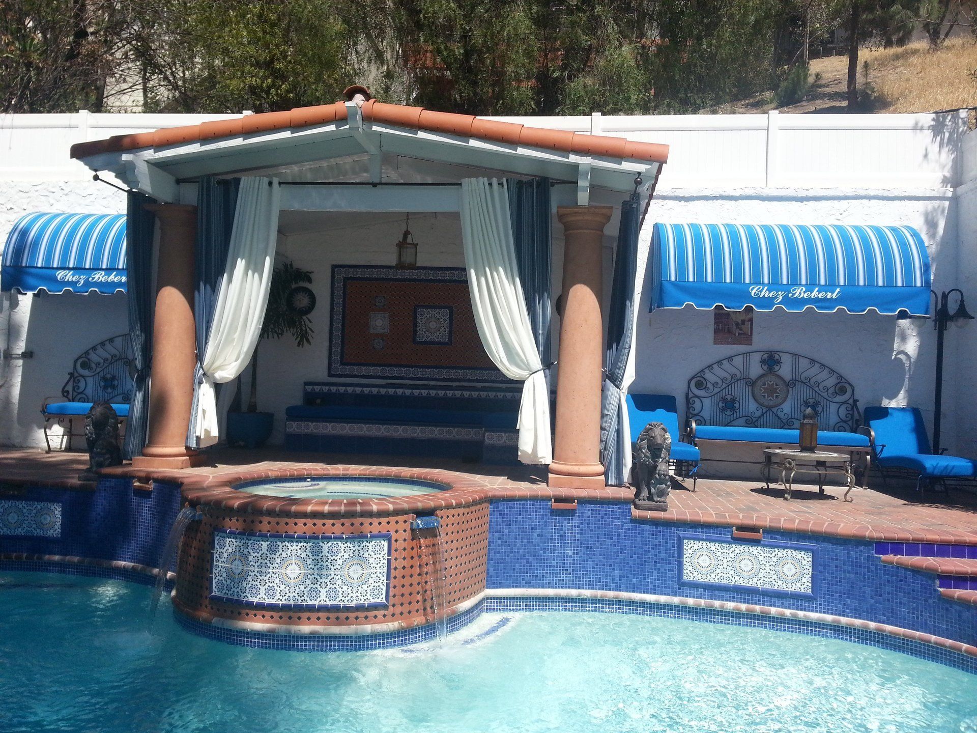 Poolside cabana with blue curtains and striped awnings beside a swimming pool