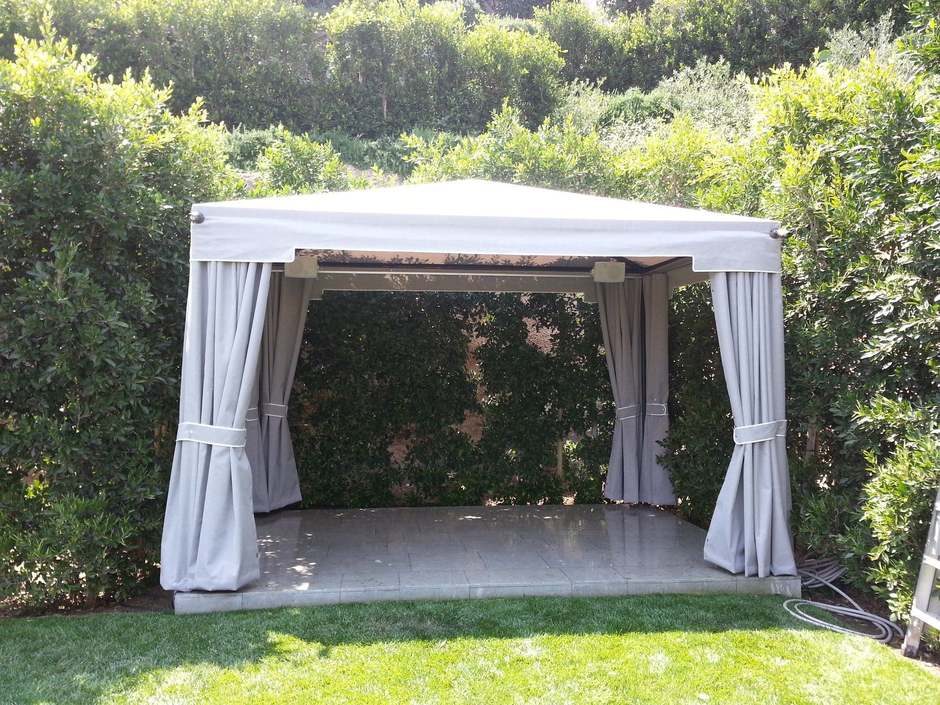 White outdoor gazebo with draped curtains in a lush green garden area