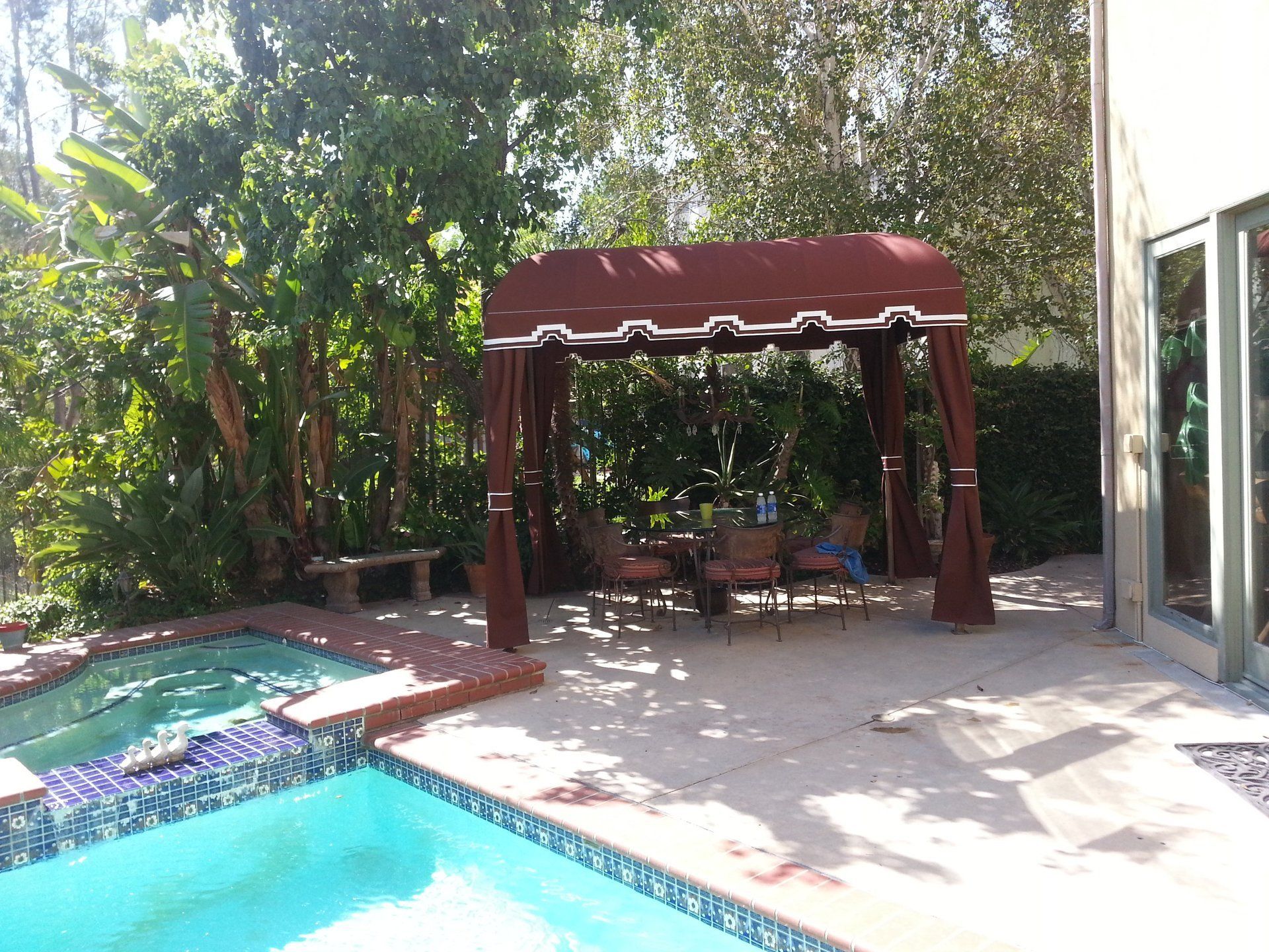 Backyard patio with red canopy gazebo beside a swimming pool and lush greenery