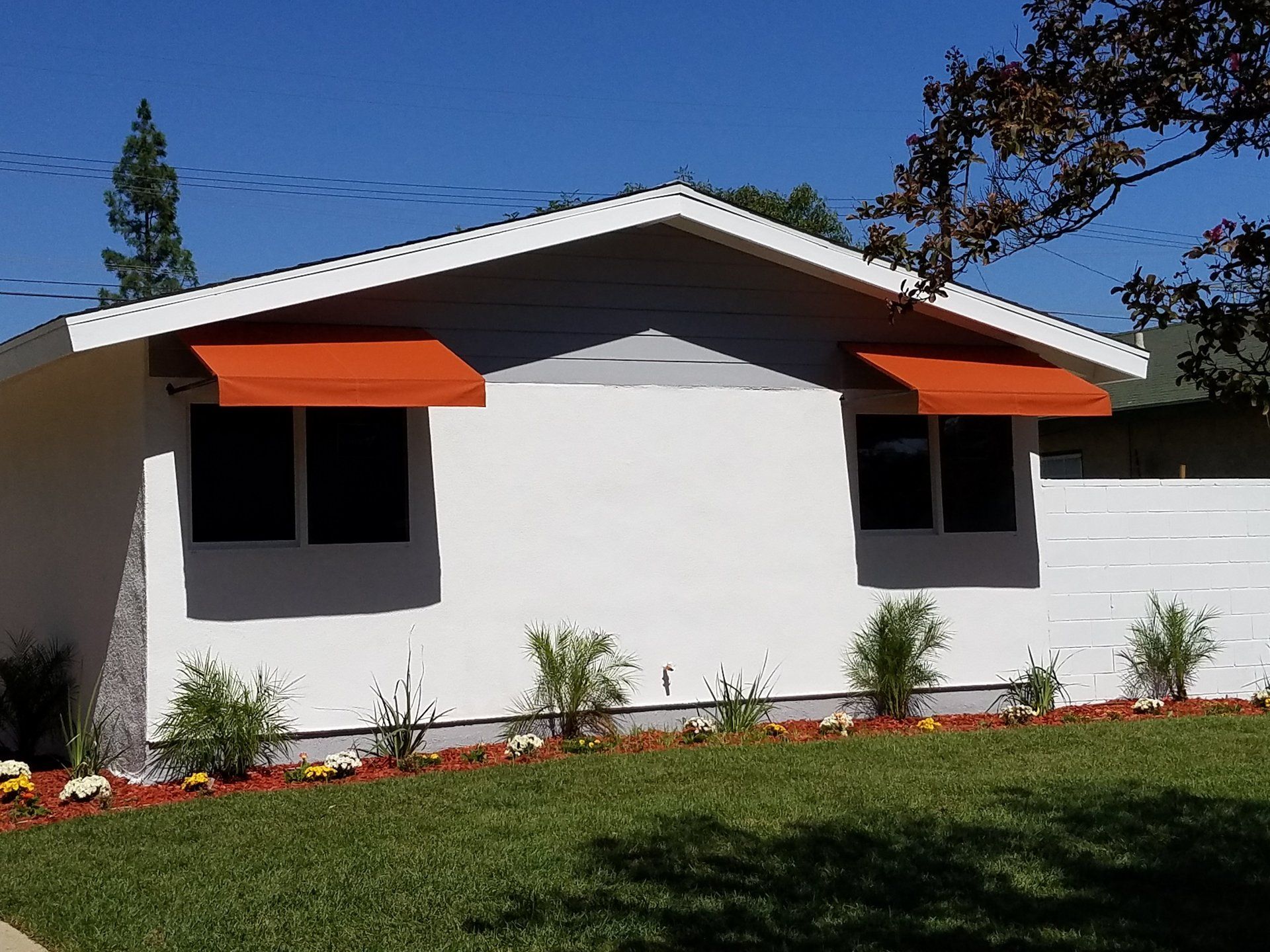 Small white house with orange window awnings, a gray roof, and a green lawn under a blue sky.