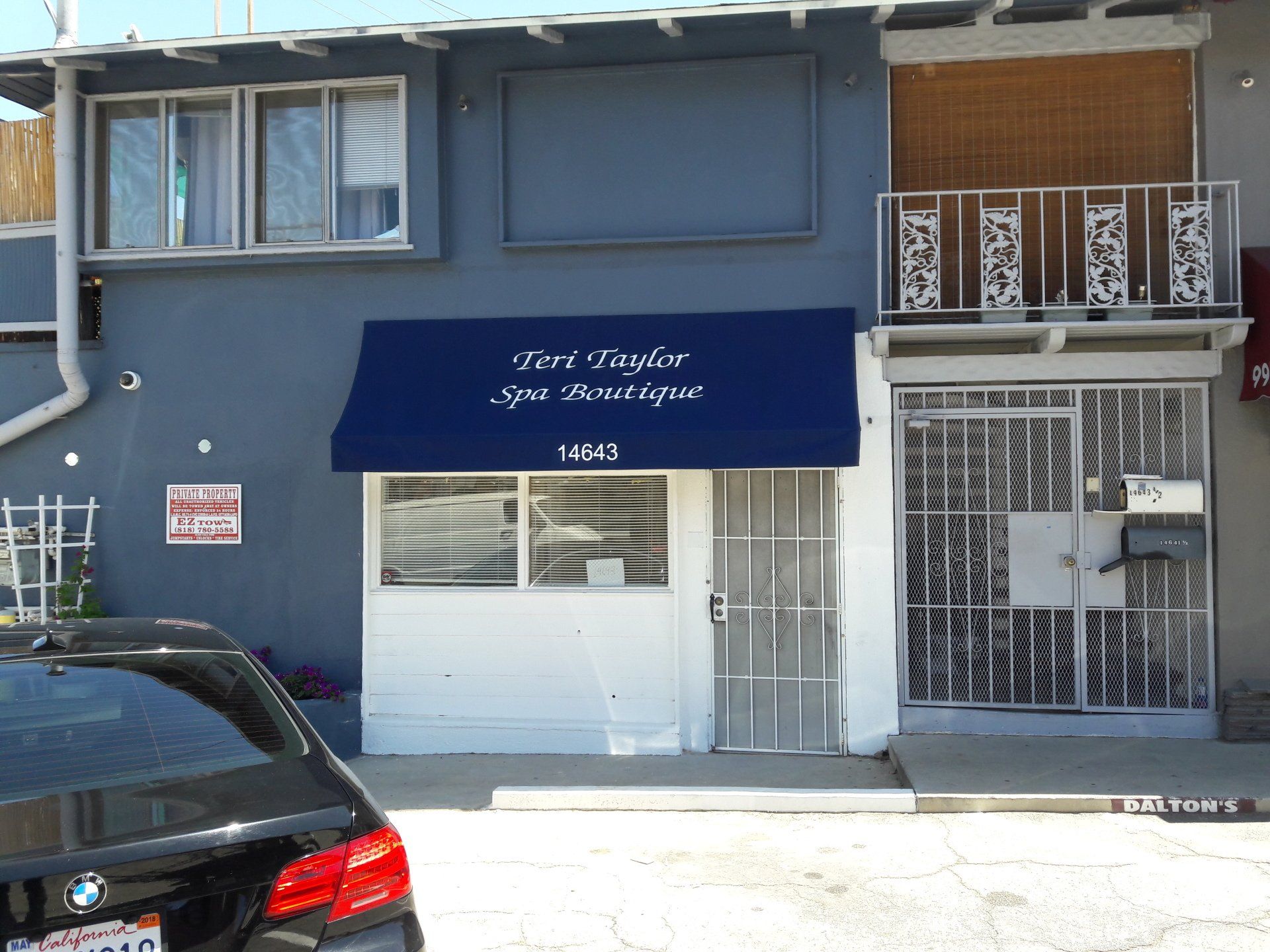 Storefront with blue awning, white garage door, and parked black car on a city street.