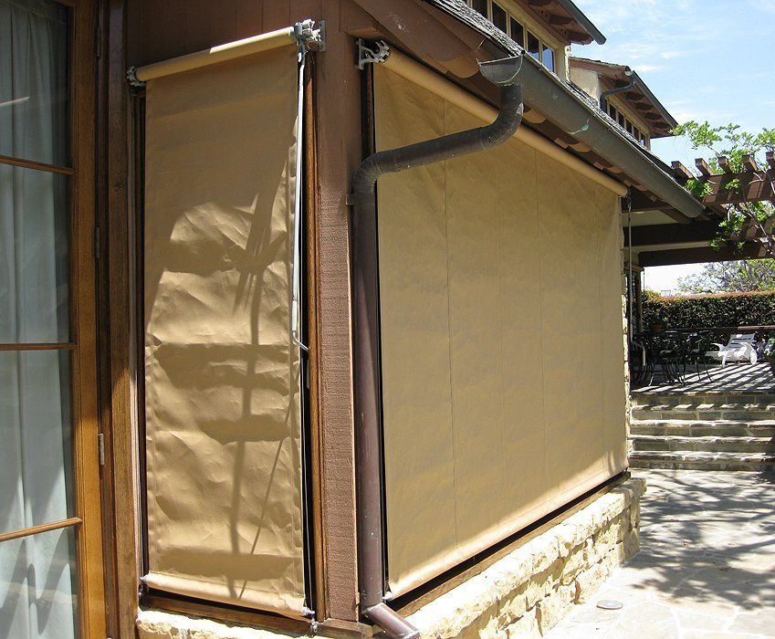 Tan fabric roll-up awning covering a building’s side wall, beside steps and a narrow outdoor walkway