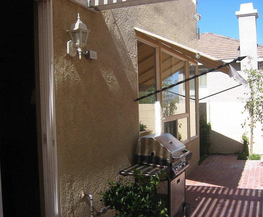 Courtyard patio with stucco wall, mounted light, grill, and brick walkway beside a glass door and awning