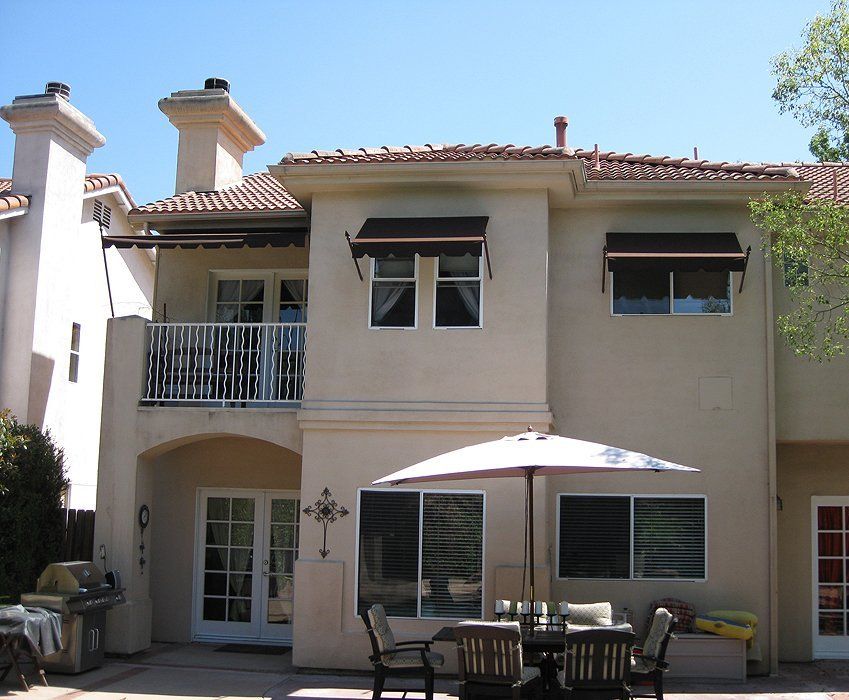 Two-story beige house with balcony and patio table under a white umbrella