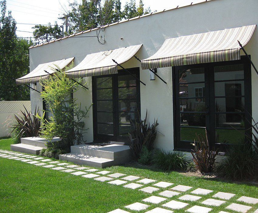 Small white house with striped awnings, front steps, and a green lawn with stepping stones.