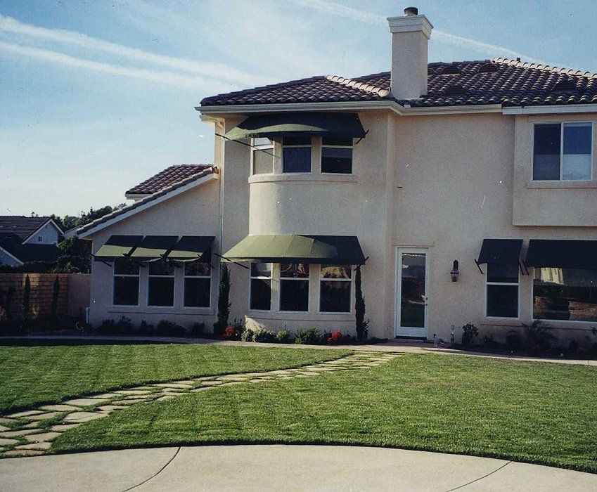Suburban two-story cream house with green awnings, tiled roof, and a front lawn in daylight