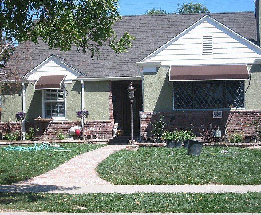 Single-story suburban house with green siding, brick accents, awnings, and a front walkway.