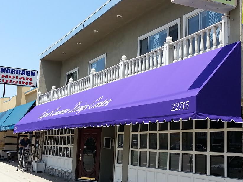 Storefront with a purple awning and white railings on a sunny street corner