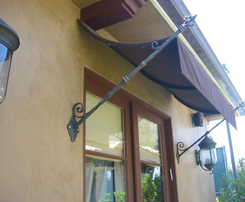 Tan awning over a stucco building entrance with window, wooden door, and wall lanterns