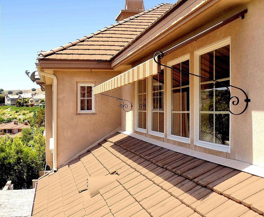 Sunlit beige house exterior with terracotta roof and striped awning over large windows