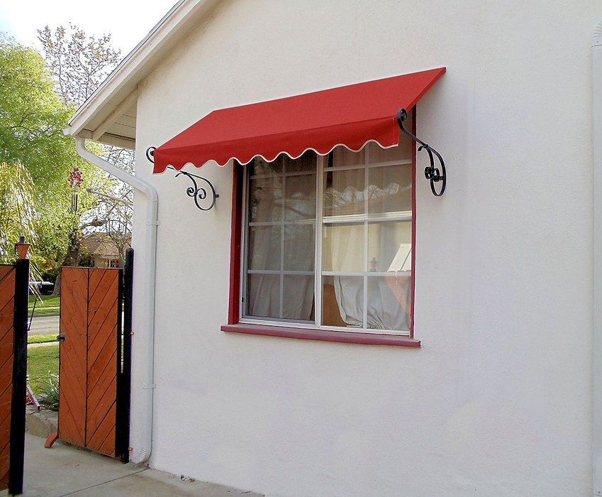 White house exterior with a red window awning and red-trimmed window beside a gate