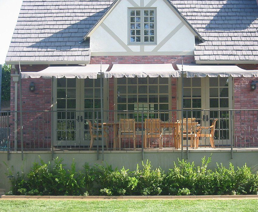 Brick house porch with patio table and chairs, white awning, and green lawn in front.