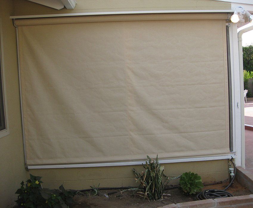 Beige outdoor window shade covering a large window on a house wall.