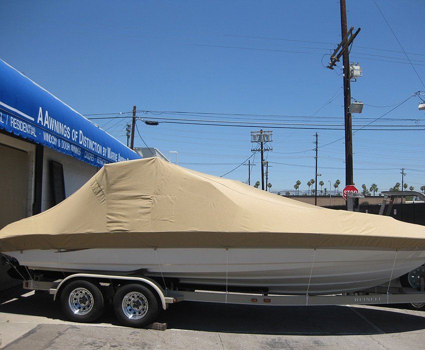 Tan-covered boat on a trailer parked beside a storefront under a blue sky