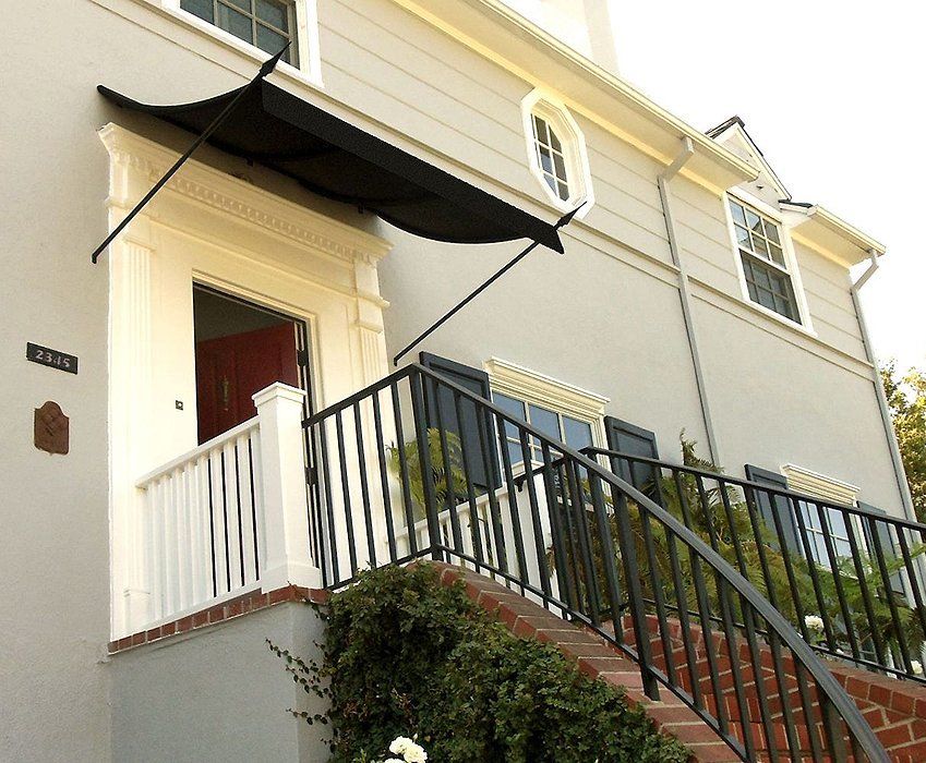 Front entrance of a cream house with red door, black awning, and staircase with black railing