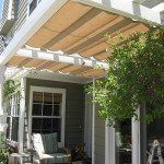 Patio with wooden pergola, white columns, and green climbing vines beside a house entrance