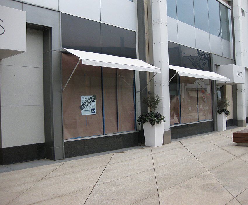Storefront windows covered with brown paper and white awnings along a modern building sidewalk