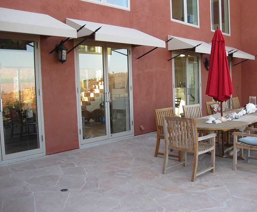 Patio with wooden dining table, red umbrella, and glass doors beside a pink stucco building