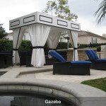 Outdoor cabana with white curtains, black lounge chairs, and blue cushions beside a pool