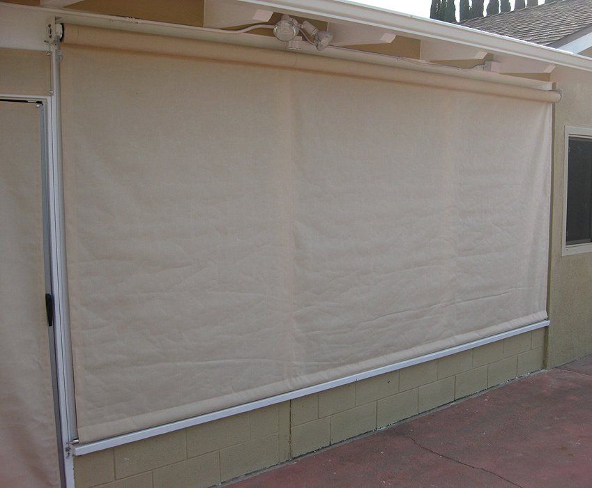 Beige outdoor roll-up shade covering a patio opening on a wall
