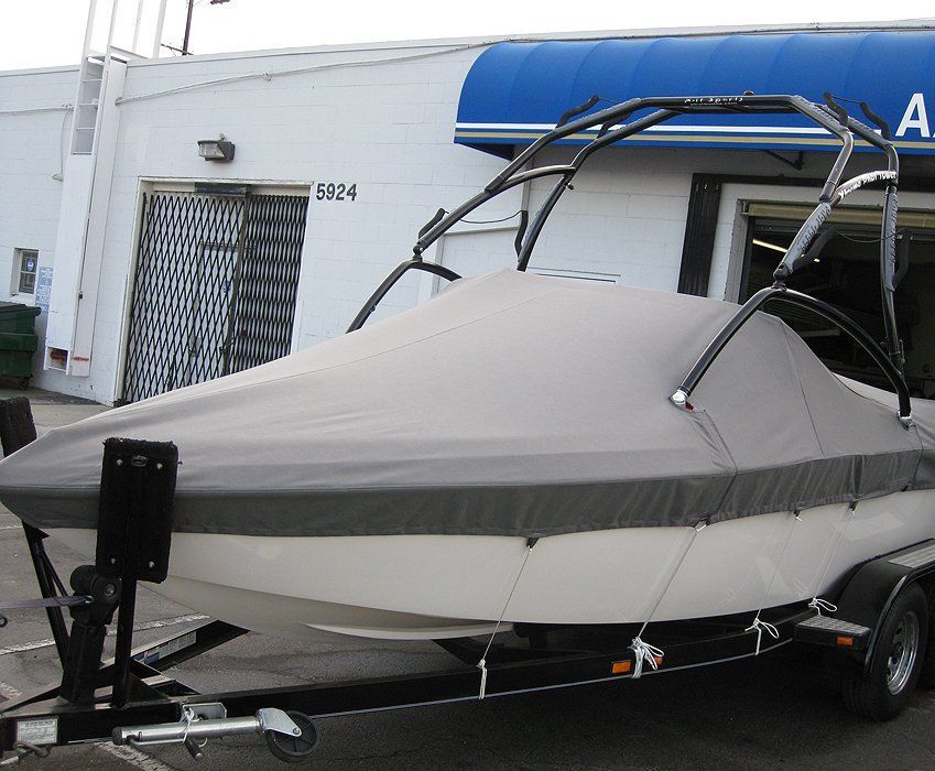Covered boat on a trailer parked beside a white building with a blue awning