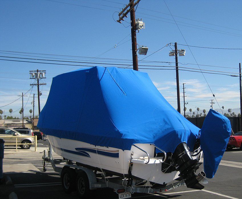 Boat covered in blue tarp on a trailer in a parking lot under a clear sky