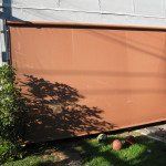 Orange privacy screen on a fence beside a white wall, with tree shadows and a small lawn.