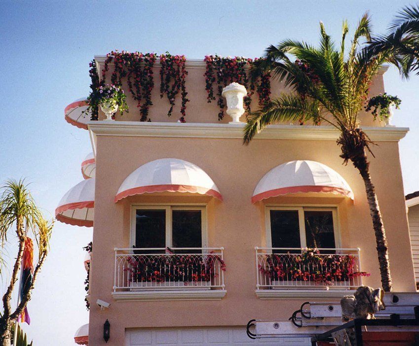 Pink stucco building with red awnings, balconies, and palm trees against a blue sky