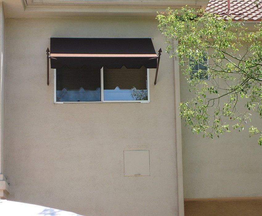 Beige building wall with a black window awning and tree branches at right.