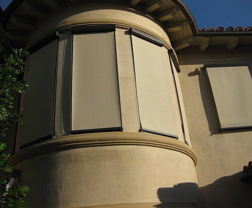 Exterior corner of a stucco house with a rounded bay window and beige shutters under a tiled roof.
