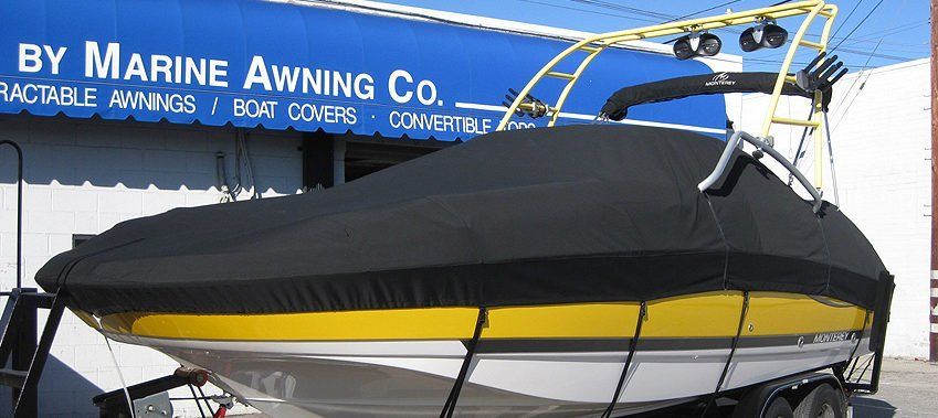 Covered white sailboat on trailer in front of blue Marine Awning Co. sign