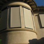 Curved beige stucco building facade with closed windows in warm sunlight