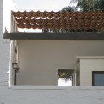 White building with a tiled awning and a small window opening, viewed from a balcony.