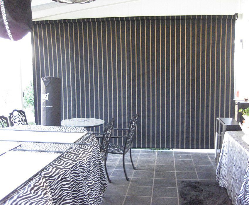 Covered patio with dark vertical blinds, tiled floor, table, and metal chairs