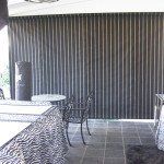 Outdoor patio with dark vertical blinds, tiled floor, and a wicker table and chairs under a white awning