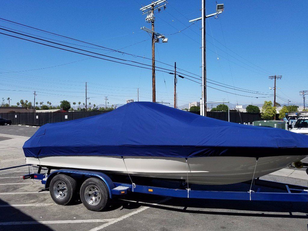 Blue covered boat on a trailer in a parking lot, with utility poles and a clear sky in the background