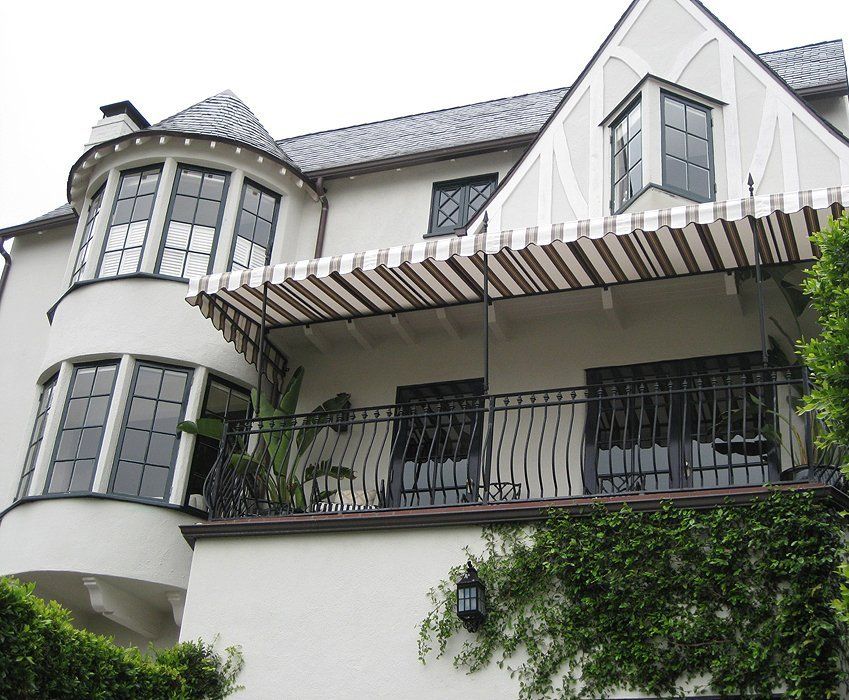 White house with arched windows, black balcony railing, and striped awning covered in ivy.