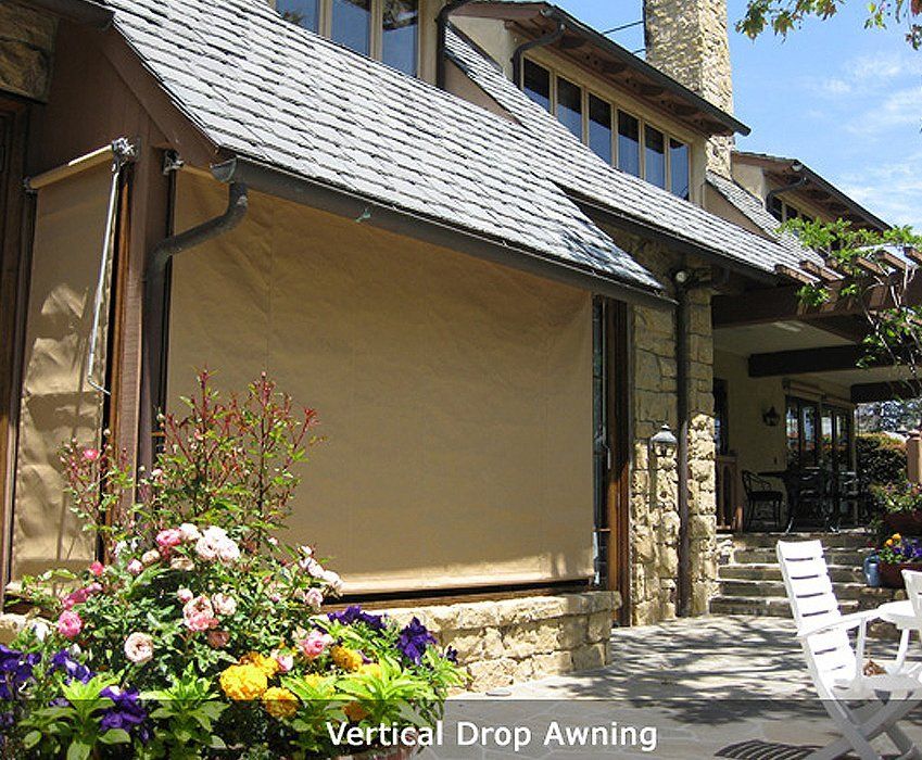 Vertical drop awning on a stone-and-wood building beside pink flowers and a walkway.
