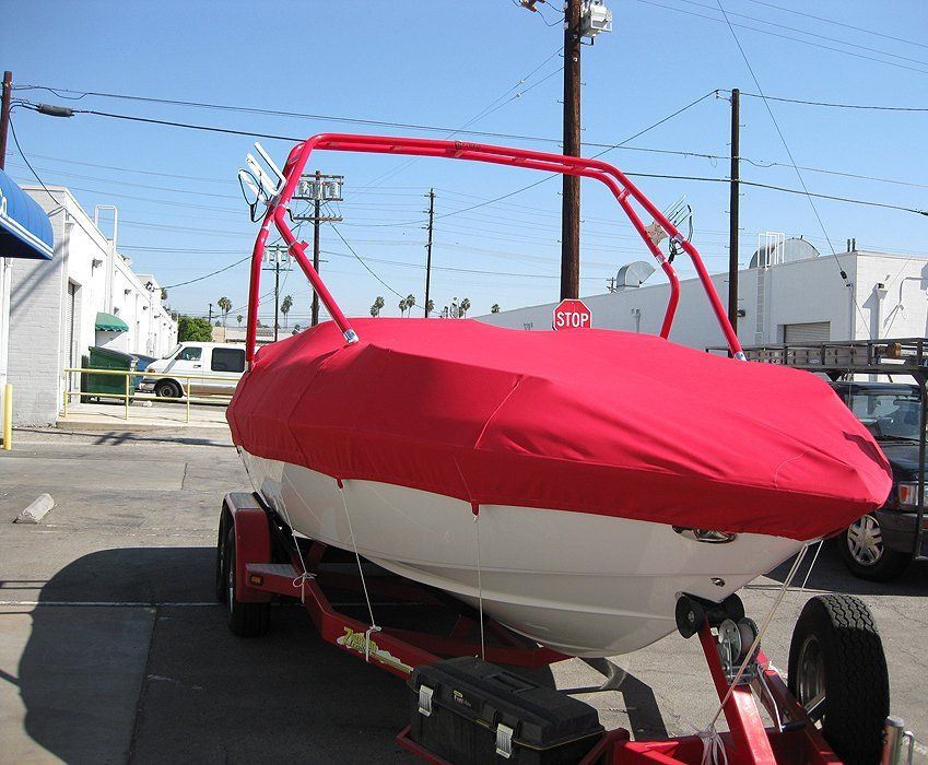 Red and white sailboat on a trailer in a parking lot under a clear blue sky.