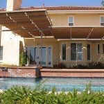 Backyard pool with beige house, covered patio, and brick wall under a tiled roof