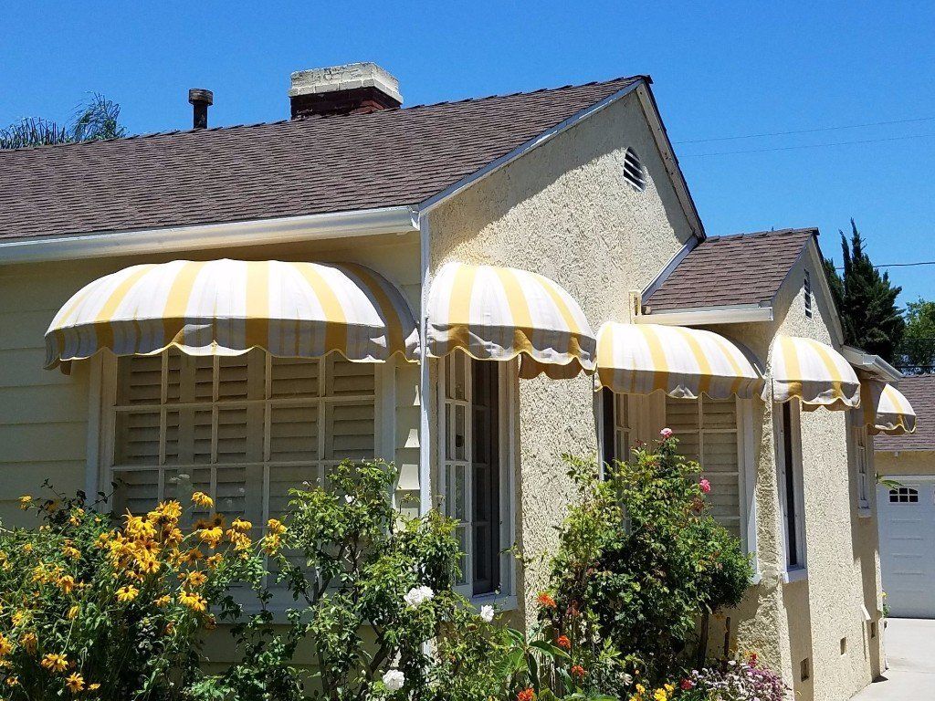 Small stucco house with yellow-and-white striped awnings, flowers in front, and a blue sky above
