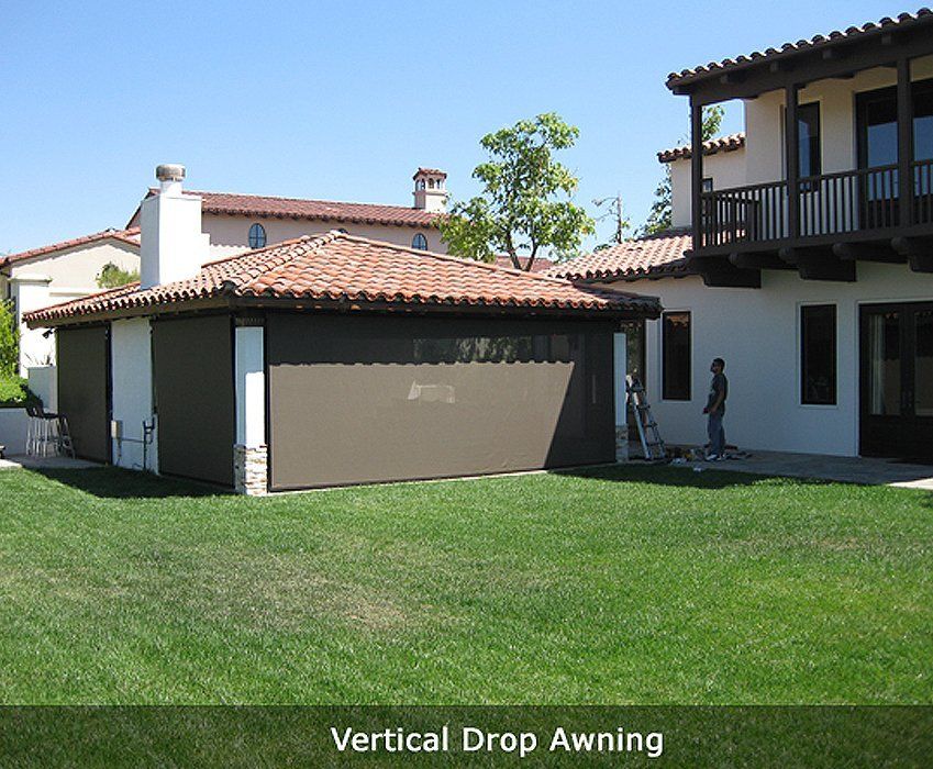 House with vertical drop awning over garage, next to a balcony and green lawn